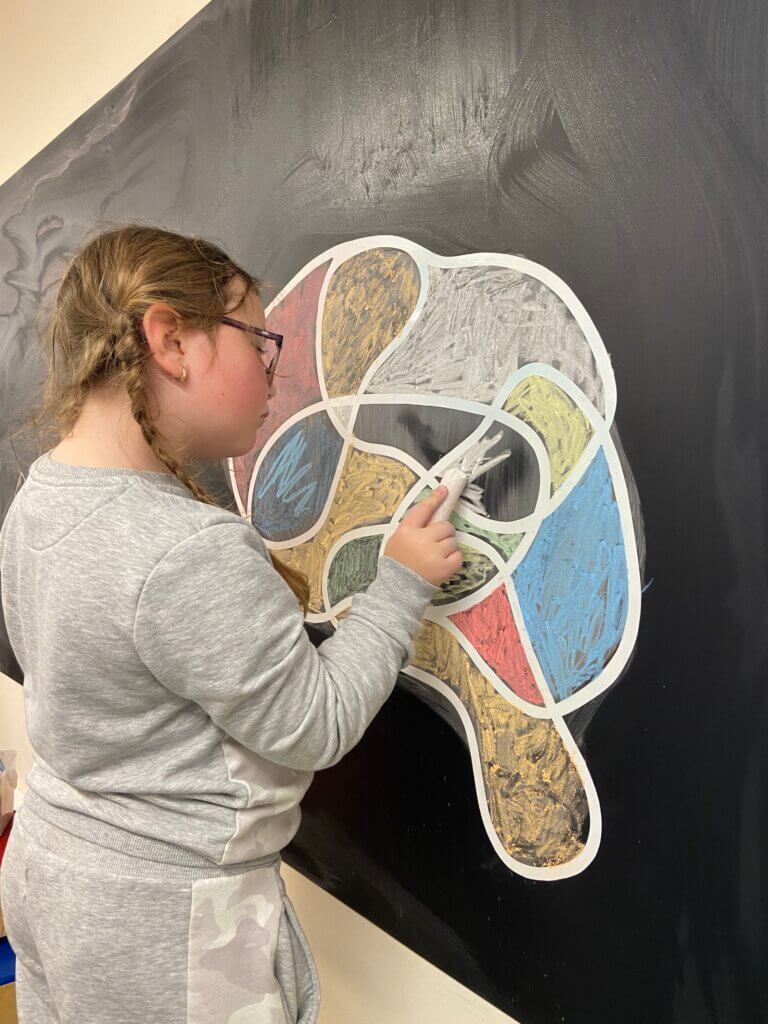 young girl colouring in bibic logo with chalk on blackboard